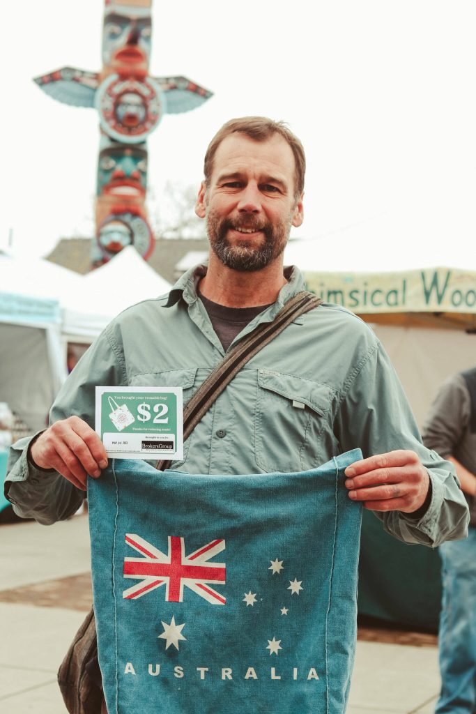 Photo courtesy Sequim Farmers & Artisans Market/ Market guest Tracy proudly shows off their re-usable bag and re-usable bag voucher, an initiative with BrokersGroup Real Estate that saves waste and keeps funds in the local economy.