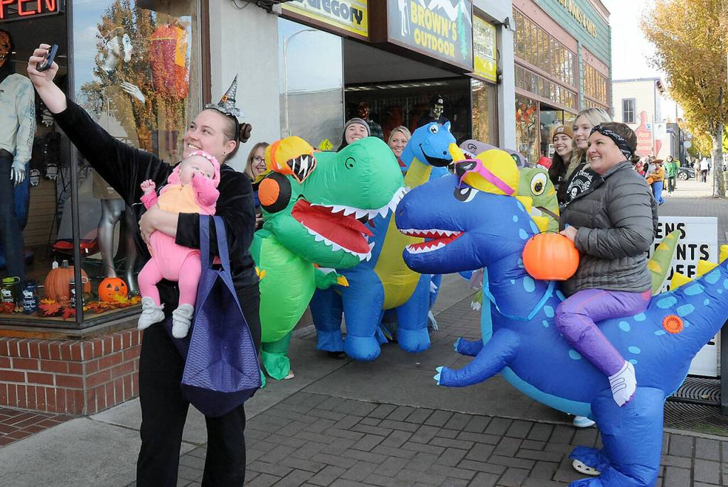 Keith Thorpe/Olympic Peninsula News Group/ Jessica Jackson of Joyce, and her son, Blakely Baker, 5 months, poses for a selfie with a herd of inflatable dinosaurs ridden by employees of Port Angeles-based Eleven Eleven Dental during Tuesdays Halloween trick-or-treating in downtown Port Angeles. Riders, were, from left, Erica Ostteen, Taylor Peabody, Krystal Feris, Emma Lindberg, Kelly Wheeleer and Alexis Perry.