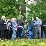 Sequim Gazette photo by Michael Dashiell / Betsy Reed Schultz (with scissors), founder of Captain Joseph House, cuts a ceremonial ribbon for a recently-donated a carved bear from Bret Wirtas Black Bear Diner and Holiday Inn & Suites.