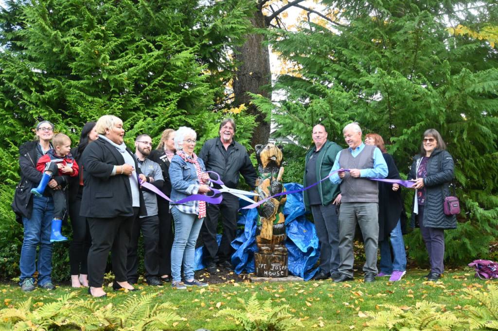 Sequim Gazette photo by Michael Dashiell / Betsy Reed Schultz (with scissors), founder of Captain Joseph House, cuts a ceremonial ribbon for a recently-donated a carved bear from Bret Wirtas Black Bear Diner and Holiday Inn & Suites.