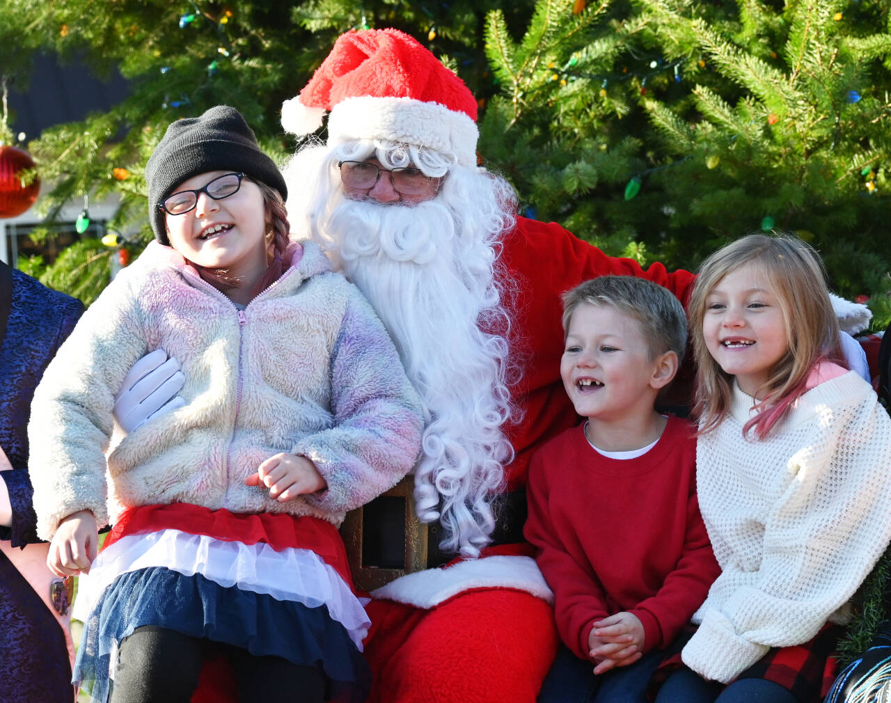 Sequim Gazette photo by Michael Dashiell / from left, Destiny, 7, Seth, 4, and Nora Summers, 6, of Sequim enjoy a moment with Santa Claus  who looks suspiciously like Stephen Rosales  at the Sequim Hometown Holidays event on Nov. 25.