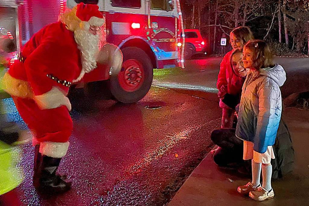 Sequim Gazette photo by Matthew Nash/ Santa Claus greets Emily Klatt and her daughters Elle and Eden Kazerouninia during Santas Toy and Food Brigades tour across Sequim on Dec. 6.