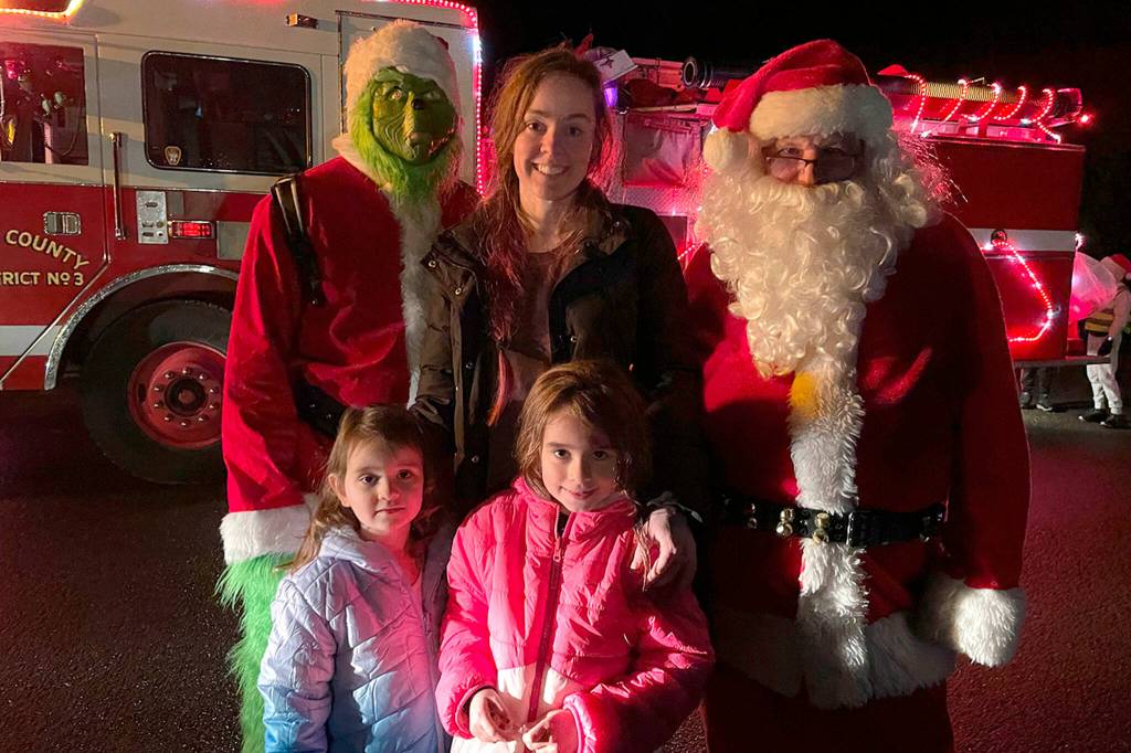 Sequim Gazette photo by Matthew Nash/ The Grinch and Santa Claus take a moment for a photo with mom Emily Klatt and daughters Elle and Eden Kazerouninia during Santas Toy and Food Brigades tour across Sequim on Dec. 6.