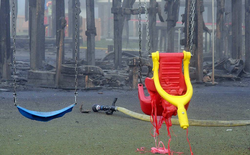 A melted infant swing hangs near a fire hose at the site of the burned Dream Playground at Erickson Playfield on Wednesday morning. (Keith Thorpe/Peninsula Daily News)