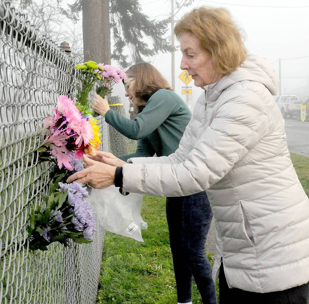 Photo by Keith Thorpe/Olympic Peninsula News Group / A melted infant swing hangs near a fire hose at the site of the burned Dream Playground at Erickson Playfield on Dec. 20.
Photo by Keith Thorpe/Olympic Peninsula News Group / Peggy DeYoung, front, and Colleen Pedersen, both of Port Angeles, place flowers on the perimeter fence of Erickson Playfield near the Dream Playground on Dec. 20.