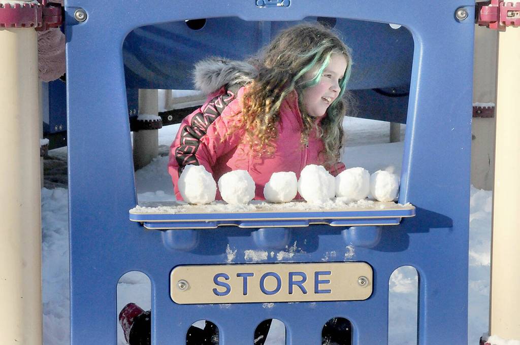 Photo by Keith Thorpe/Olympic Peninsula News Group / Madrona Villella, 7, of Port Angeles looks out from a pretend storefront lined with snowballs at the childrens playground at Shane Park on Jan. 12 in Port Angeles. The youngster braved single-digit wind chills for a chance at a snow day in the park.