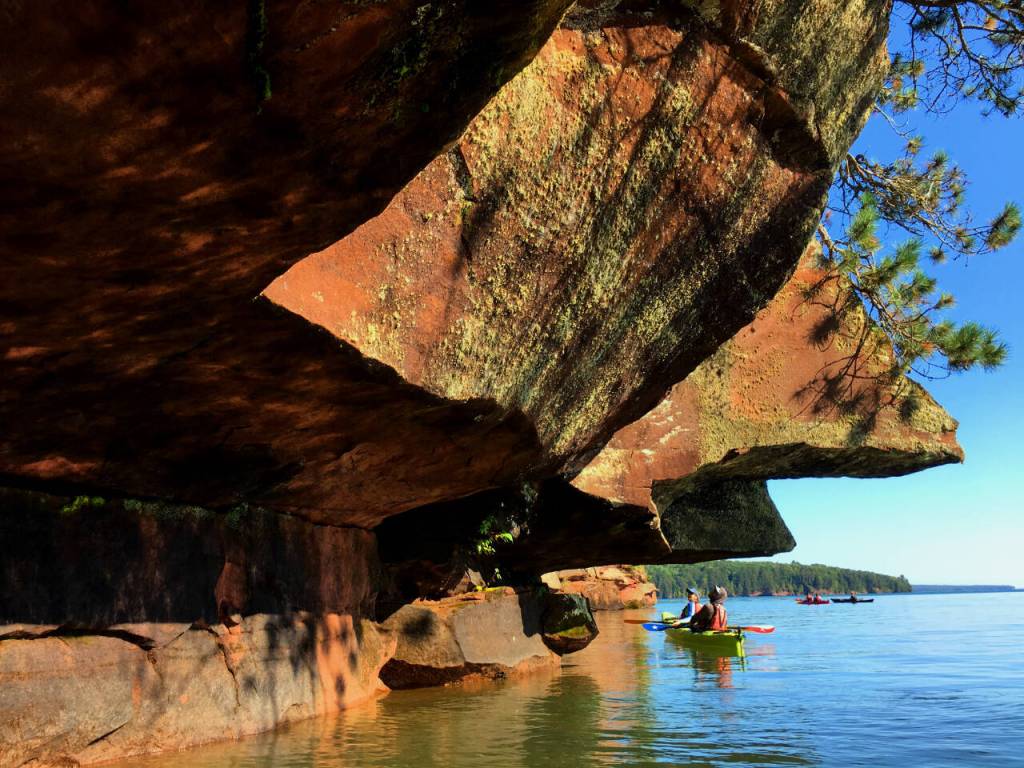 Photo courtesy of Gail Green and Grant Herman / Kayakers get an up-close look at an overhanging cliff near one of Lake Superiors Apostle Islands.