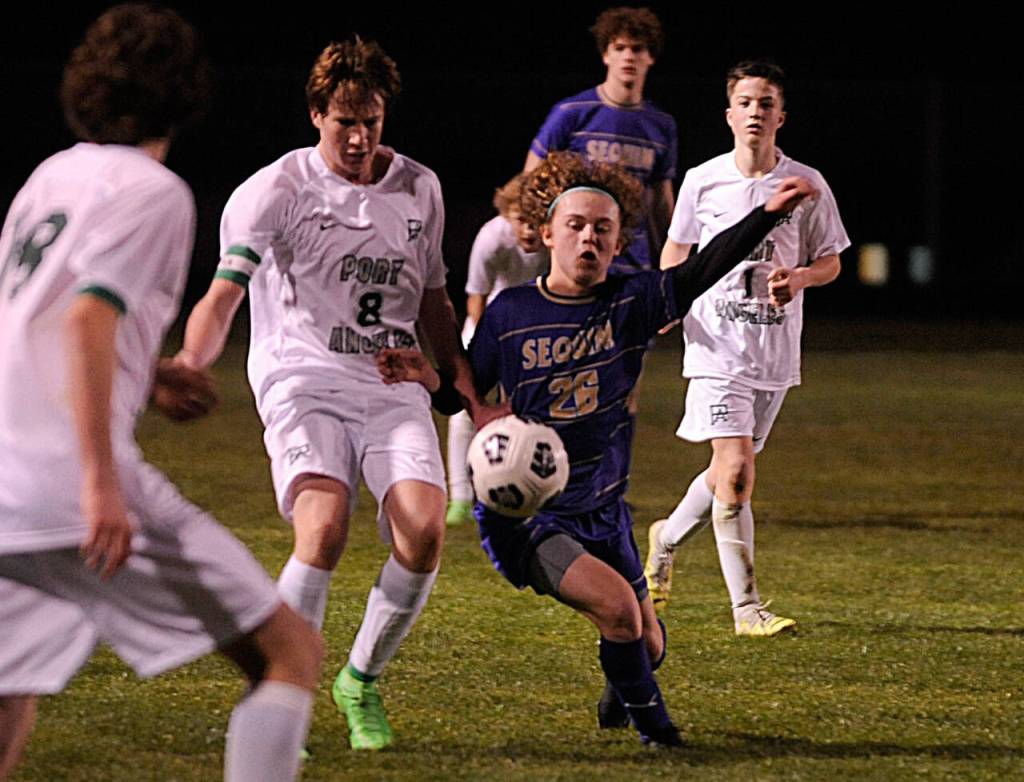 Sequim Gazette photo by Matthew Nash / Sequims Max Stanford, center, vies for the ball with Port Angeles Jacob Weaver in SHSs season-opening 4-2 win on March 14.