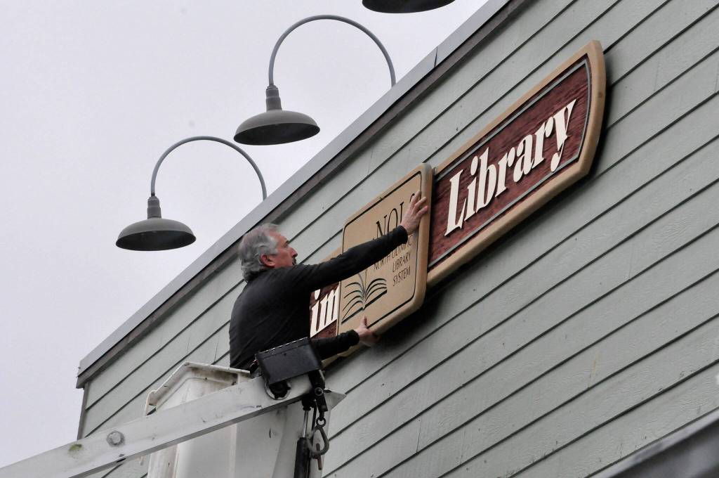Sequim Gazette photo by Matthew Nash
Bruce Miller, owner of Miller Signs, places the Sequim Library sign on March 22 outside the temporary building at 609 W. Washington St., Suite 21. Miller Signs former owner Rob Campbell built the sign in 2009 for the remodel of the current library at 630 N. Sequim Ave. The library is set for expansion and renovation through the next year.