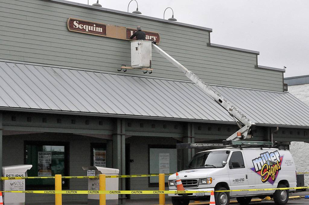 Sequim Gazette photo by Matthew Nash/ Bruce Miller, owner of Miller Signs, places the Sequim Library sign on March 22 outside the temporary building at 609 W. Washington St., Suite 21. Miller Signs former owner Rob Campbell built the sign in 2009 for the remodel of the current library at 630 N. Sequim Ave. The library is set for expansion and renovation through the next year.