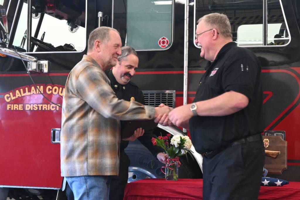 Sequim Gazette photo by Michael Dashiell / Outgoing District 3 interim chief Dan Orr gets a hearty thanks from current chief Justin Grider; deputy chief Tony Hudson is in the background.
