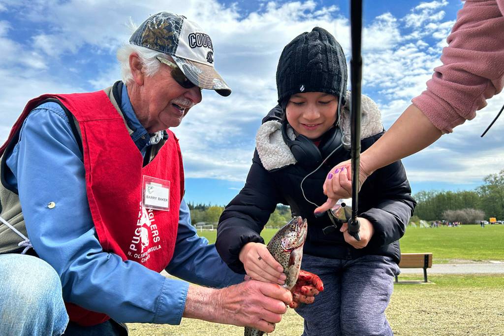 Barry Baker, a volunteer with the North Olympic Peninsula Chapter of Puget Sound Anglers, helps Christian Stevenson, 11, of Port Ludlow, take the hook out of his recently caught fish at Kids Fishing Day. It was Stevensons second fish of the day, he said.