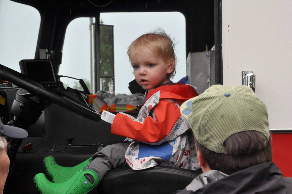Two-year-old Ozzie Herbert sits in a fire engine courtesy Clallam County Fire District 3 as his dad Teddy watches him.