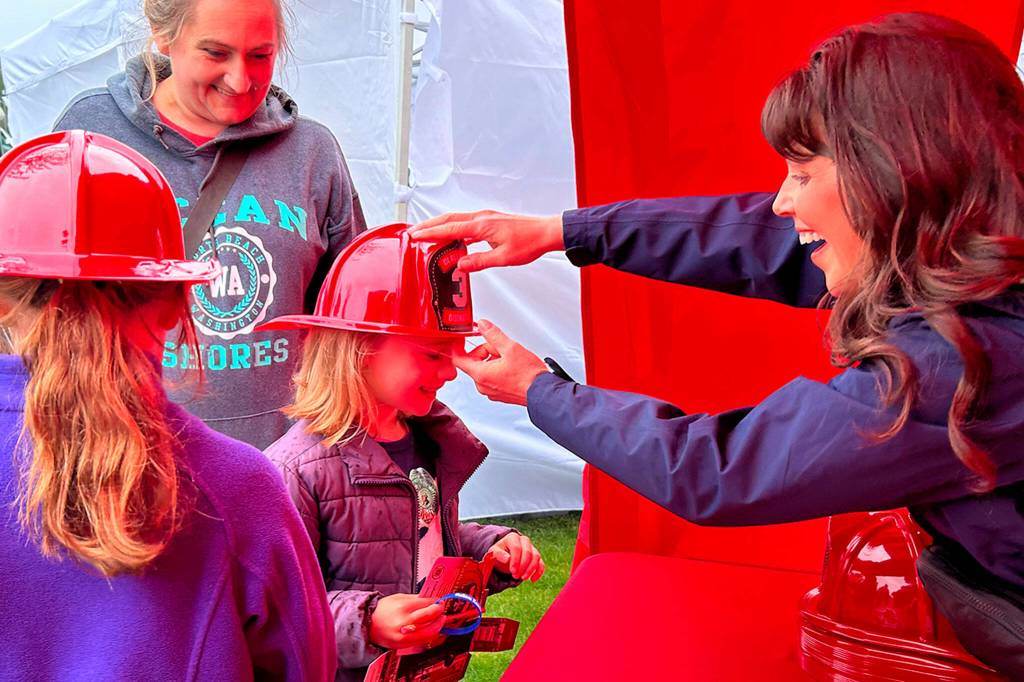 Kylynn Hibbard, 7, receives a fire hat from Lori Coleman, an executive assistant with Clallam County Fire District 3, during Family Fun Days as Kylynns mom Maria and sister Ryah, 8, look on. The family came to see their friends and fellow dancers from The Dance Center perform, they said.