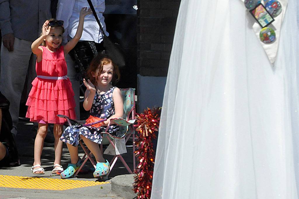 Sequim Gazette photo by Matthew Nash/ Four-year-old friends Yana White, left, and Isla Daines wave to a royalty float as it goes down Washington Street for the Grand Parade. This was Yanas second time at the parade, while Isla has gone since she was a baby, their moms said.