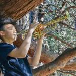 Sequim Gazette photo by Elijah Sussman / Writer Anderson Williams holds trumpet in tree before concert in bandshell at Carrie Blake Park on June 6.