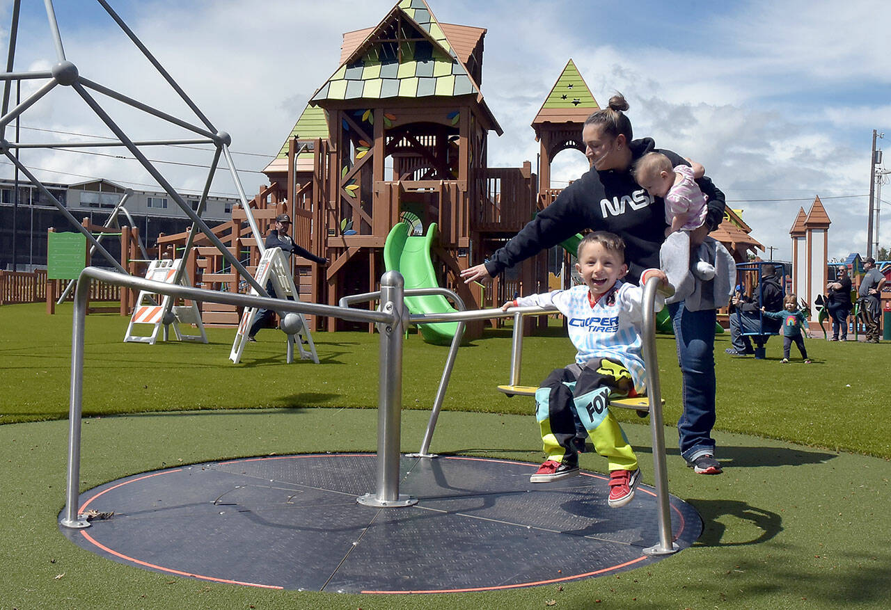 Photo by Keith Thorpe/Olympic Peninsula News Group
Three-year-old Archie Hanson takes a spin on a merry-go-round pushed by his mother, Justine Hanson of Port Angeles, with sister Arlene Hanson 7 months, during the grand reopening of the Dream Playground at Erickson Playfield in Port Angeles on June 16. The playground was rebuilt earlier this month by volunteers after an arson fire destroyed much of the playground equipment in December. Although there are still details to attend to and minor adjustments to be made, the facility will be open daily from dawn until dusk.