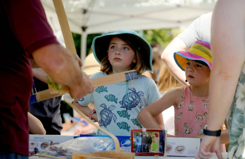 Sequim Gazette photos by Michael Dashiell
At left, Sophia Arbuckle, 9, and Grace Kirn, 7, both of Port Townsend, learn about craft stick bending from Sequims Brad Griffith at the Toy Makers Teacher booth during the City of Sequims 2024 Independence Day Celebration at Carrie Blake Community Park on July 4.