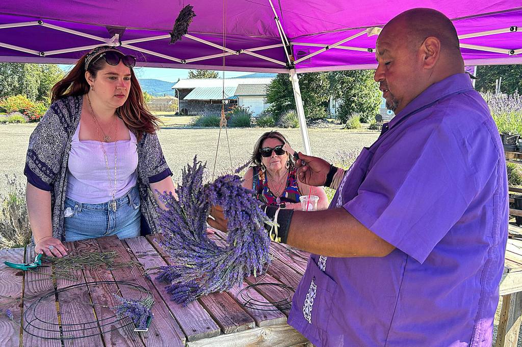 Sequim Gazette photo by Matthew Nash/ Sergio Gonzalez of Melis Lavender Farm helps Morgan Wilson of Lacey and Jolene Wilson of Birmingham, Ala., make lavender wreaths on July 20. Morgan said she recently moved to Washington and had read about Sequims lavender and it put it on her calendar to visit.
