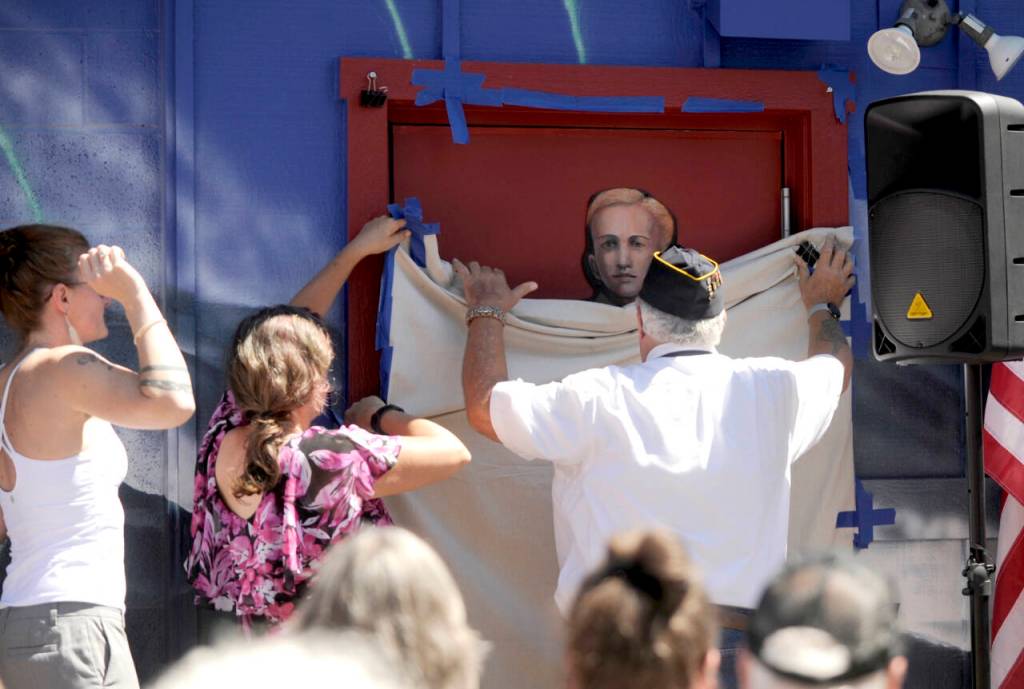 Sequim Gazette photo by Michael Dashiell / American Legion post Commander Carl Bradshaw and Sequim artist Melissa Klein unveil the portrait of Jack Grennan as Holly Rowan, president of the Clallam County Veterans Association, looks on at the July 20 unveiling of the Legions Remember Me mural.