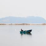 A boat floats placidly on Dungeness Bay as hikers walk along Dungeness Spit in the background and Striped Peak stands on the horizon in October 2022.