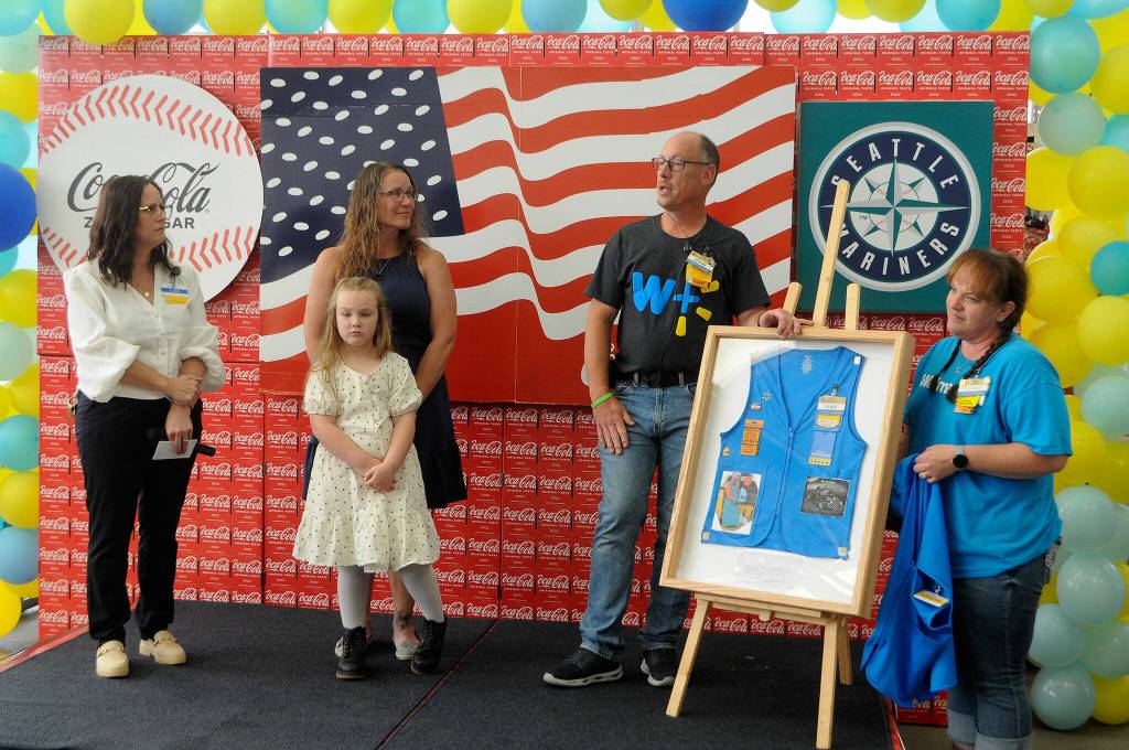 Sequim Gazette photo by Matthew Nash/ John-Paul and Jessica Davis, right, present a shadowbox of Lynie Staus work vest to his wife Donna and granddaughter Jordyn on Aug. 2 during a ceremony for the Sequim Walmarts remodel. Staus worked for Sequim Walmart since it opened.