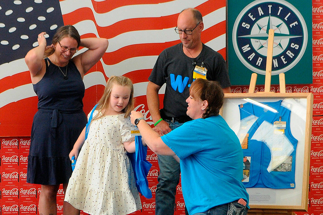 Sequim Gazette photo by Matthew Nash
Jessica Davis helps Jordyn Mancuso-Staus put on a personalized vest during the Aug. 2 ribbon cutting for the remodel of the Sequim Walmart as Jordyns grandmother Donna Staus, left, and Jessicas husband John-Paul Davis watch. The Davises presented Donna with a shadowbox with her late-husband Lynie Staus work vest. Lynie passed away May 1, shortly before his 24th anniversary with the company. See story and photos, A-4.