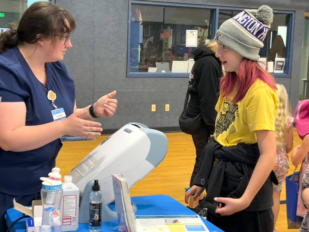 iara Amundson, a licensed optician with Sequim Walmarts Vision Center, talks with Aubrey Dailey about a vision test at the Back to School Fair. Aubreys mom Sam said her family looks forward to coming each year to the event.