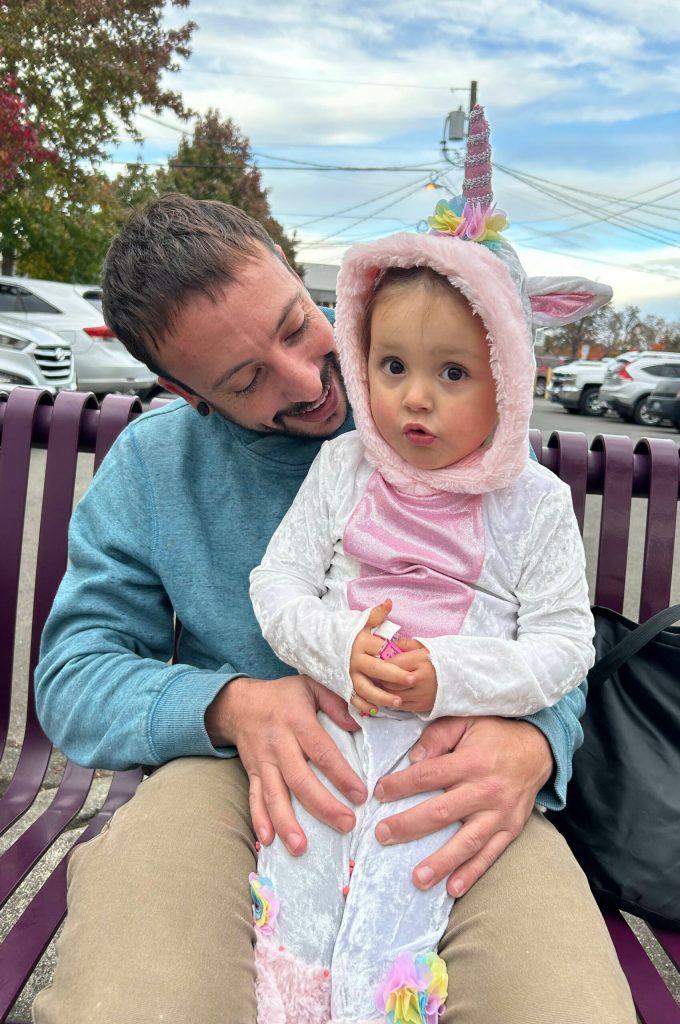 At right: John Gondek takes a break from trick-or-treating with his 3-year-old daughter Luna, dressed as a unicorn, who enjoys some candy on Halloween.