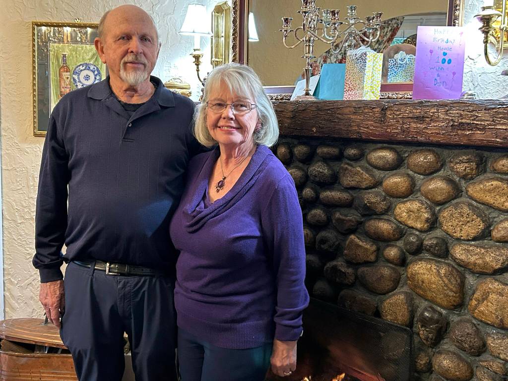Sequim Gazette photo by Matthew Nash/ Don Palm and Winnie Greenaway-Palm stand by a fireplace made with rocks from the Dungeness River during their party celebrating the 100th anniversary of their Sequim Heritage House. On their mantle sits a birthday card for the house and other congratulatory cards.