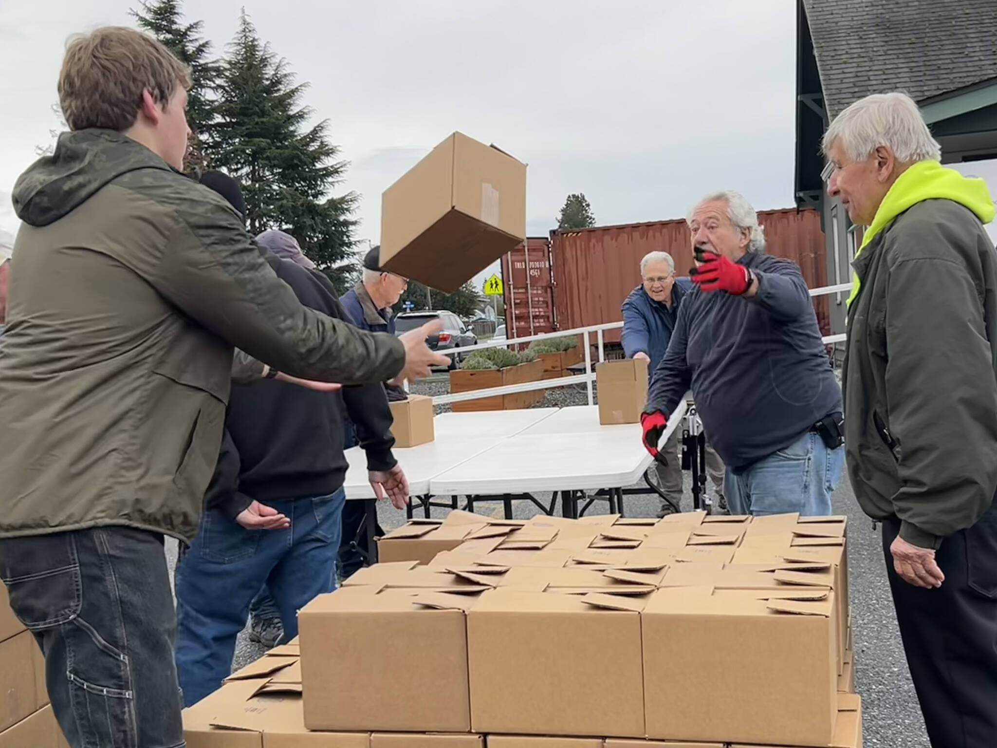 Sequim Gazette photo by Matthew Nash
Harvey Hochstetter tosses a box of food to Cameron Needham to stack on Nov. 21 with fellow volunteers like Bill Needham, on right, for the Sequim Food Banks Holiday Meal Bag Distribution event. Cameron, his father Ty and grandfather Bill were three generations helping the program.
