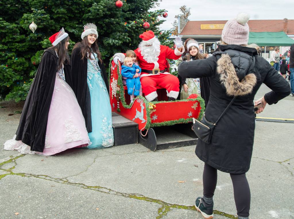 Sequim Gazette photo by Emily Matthiessen/ In a classic holiday moment, young Ben Molles, held by his sister Daisy, fails to appreciate Santa's sleigh at Hometown Holidays in Sequim on Saturday, but his mother Alexis hurries to rescue him.