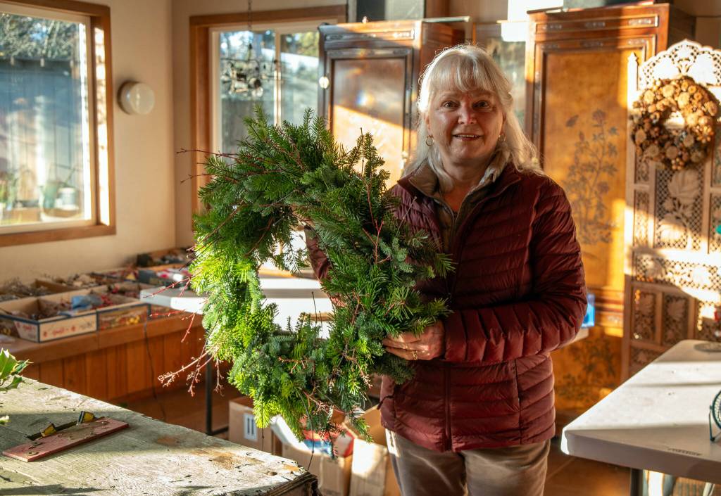 Emily Matthiessen/ Ann Johnson of Lazy J Tree Farm and two other women make Christmas wreaths in a sunlit room of the Johnson home.