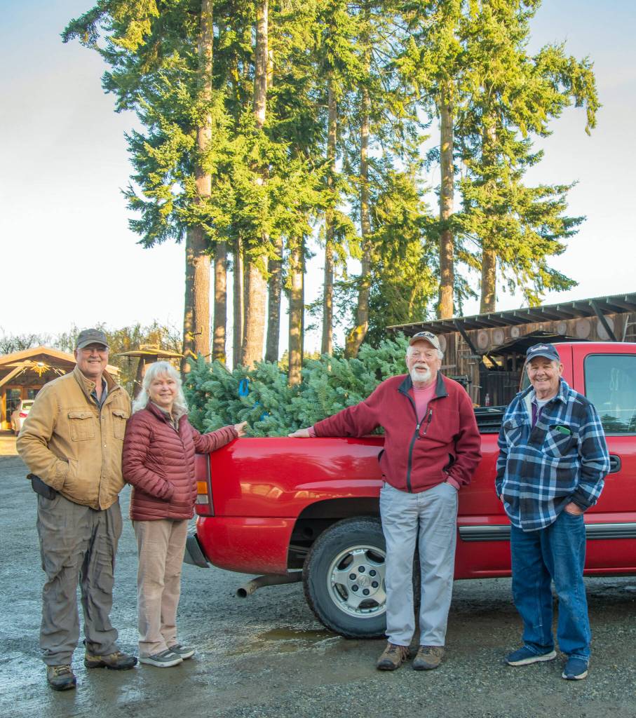 Sequim Gazette photo by Emily Matthiessen/ From right, Mark Silkas and Steve Sahnow receive a donated Noble fir from Ann and Steve Johnson at the Lazy J Tree Farm to be the Giving Tree sponsored by the Friends of Sequim outside of Habitat for Humanity, which is hung with personal care items and presents for passersby, who are also encouraged to leave behind a present.