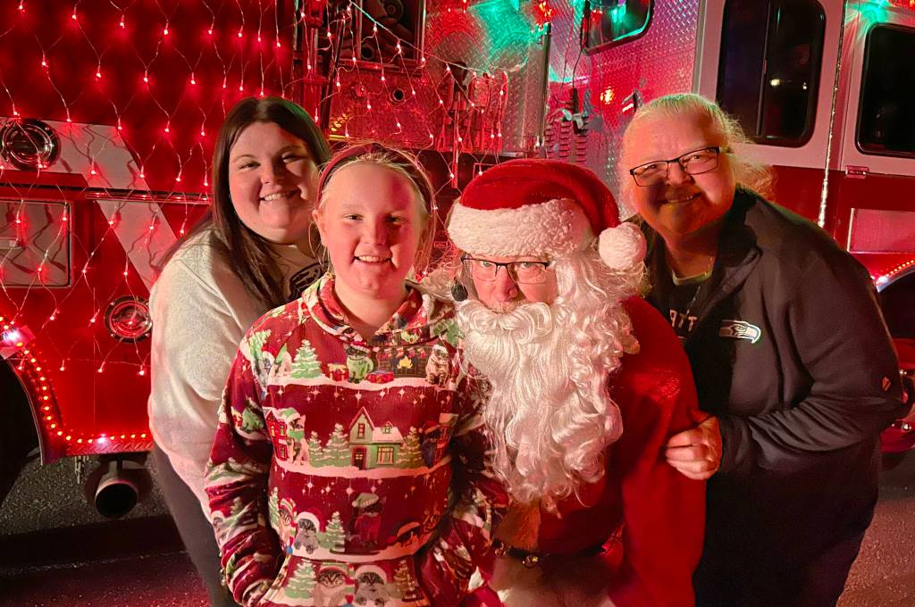 Sequim Gazette photo by Matthew Nash/ Santa (John Brygider) takes a photo with Amanda, mom, and daughter Amelia Critchfield, 10, and grandma Lisa Erickson of Vancouver on Dec. 5 during Santas Toy and Food Brigade visit on Dec. 5 in Sunland. The brigade seeks items each to support the Sequim Food Bank and Toys for Sequim Kids.