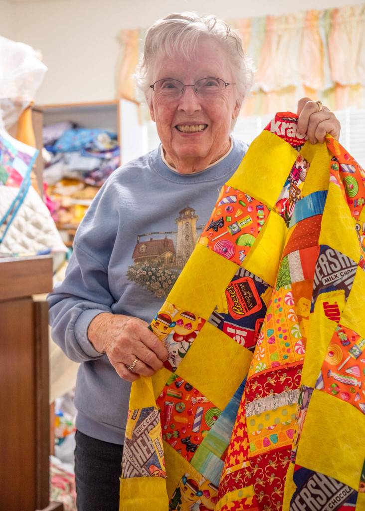 Sequim Gazette photo by Emily Matthiessen
Robirts shows the top of a childs quilt that she will give away after completing. Behind her, in her sewing room, stacks of cloth await her hands.