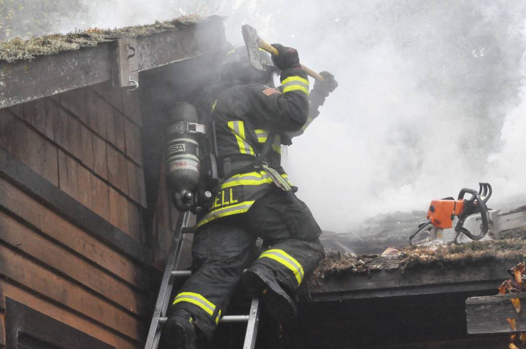 Sequim Gazette file photo by Matthew Nash/ Firefighter/EMT Tyler Campbell with Clallam County Fire District 3 vents a roof during a house fire last Nov. 12 near Sequim.