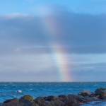 Sequim Gazette photo by Emily Matthiessen/ High waves at Cline Spit on Friday splash into the parking lot while a brief storm brings a chunk of rainbow over the sea.
