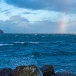 Sequim Gazette photo by Emily Matthiessen/ High waves at Cline Spit on Fri. Jan 10 splash into the parking lot while a brief storm brings a chunk of rainbow over the sea.