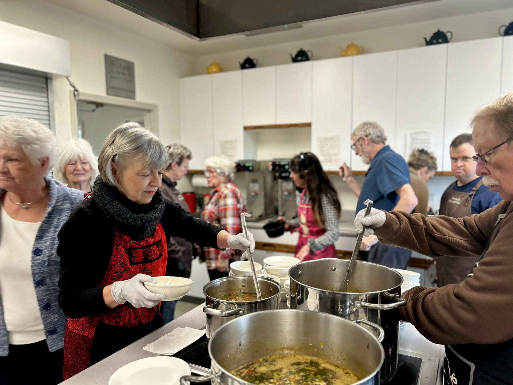 Sequim Gazette photos by Kathy Cruz
At noon every Wednesday, the kitchen at St. Lukes Episcopal Church in Sequim is a flurry of activity as volunteers begin serving a free lunch that consists of hot soup, salad, a bread item (yeast rolls, biscuits or corn muffins and a dessert. Here, the cooking team of Janet Popelka and Ray Kaminsky ladle soup into bowls as other volunteers bustle around them.