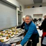 Volunteer Isabelle Mackiewicz places biscuits on plates minutes before the kitchen window was opened to allow servers to distribute food to guests sitting at tables decorated with fresh flowers, white tablecloths and cloth napkins.