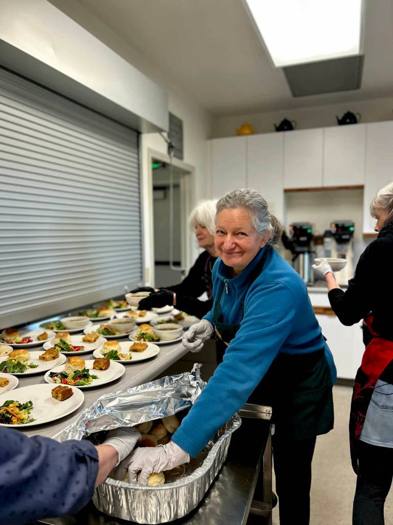 Volunteer Isabelle Mackiewicz places biscuits on plates minutes before the kitchen window was opened to allow servers to distribute food to guests sitting at tables decorated with fresh flowers, white tablecloths and cloth napkins.