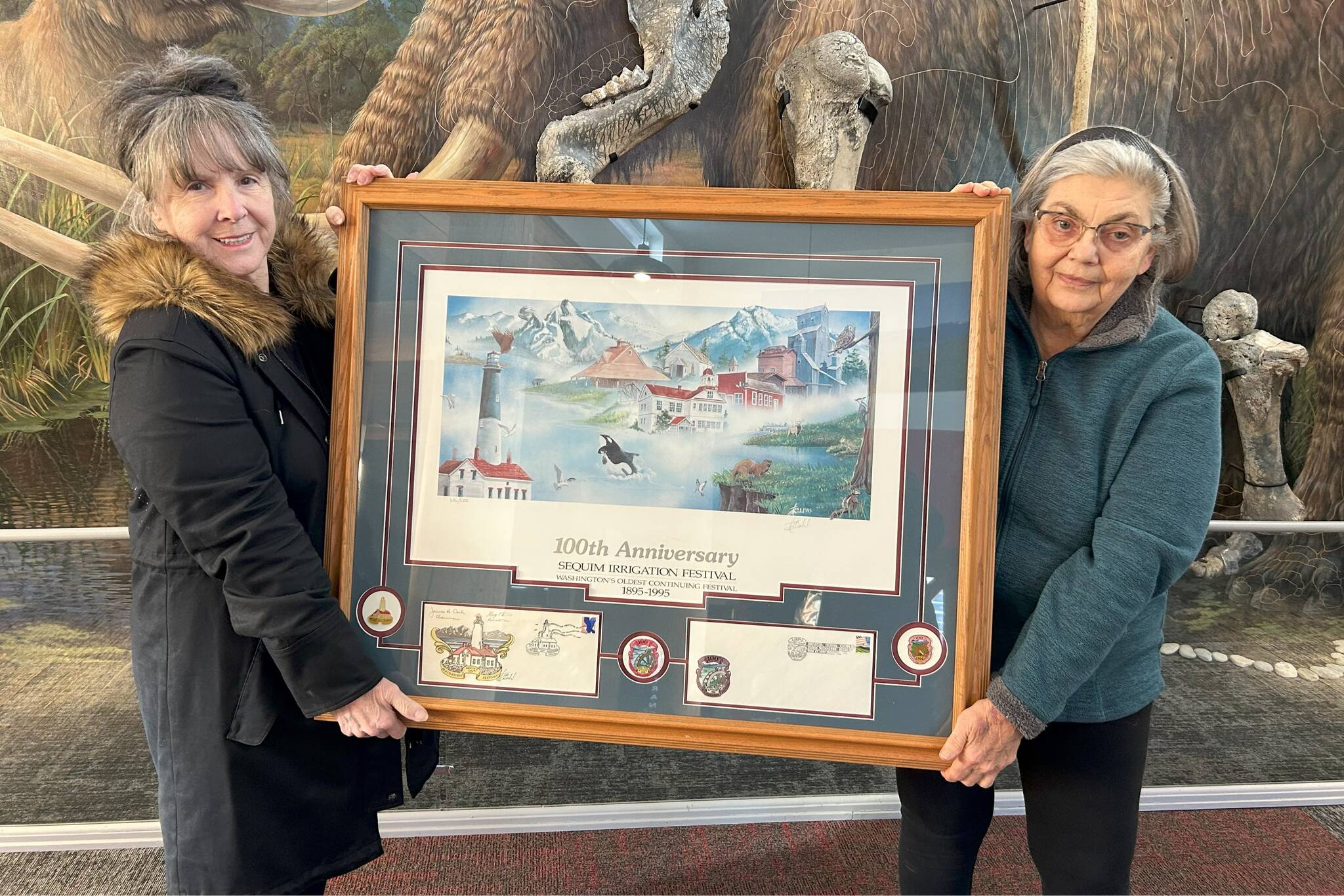 Sequim Gazette photo by Matthew Nash
Executive Director Judith Reandeau Stipe and board member Beverly Majors with Sequim Museum & Arts hold a large Tim Quinn print commemorating the 100th anniversary of the Sequim Irrigation Festival that will be auctioned off during the month of February in a silent auction in the museum.