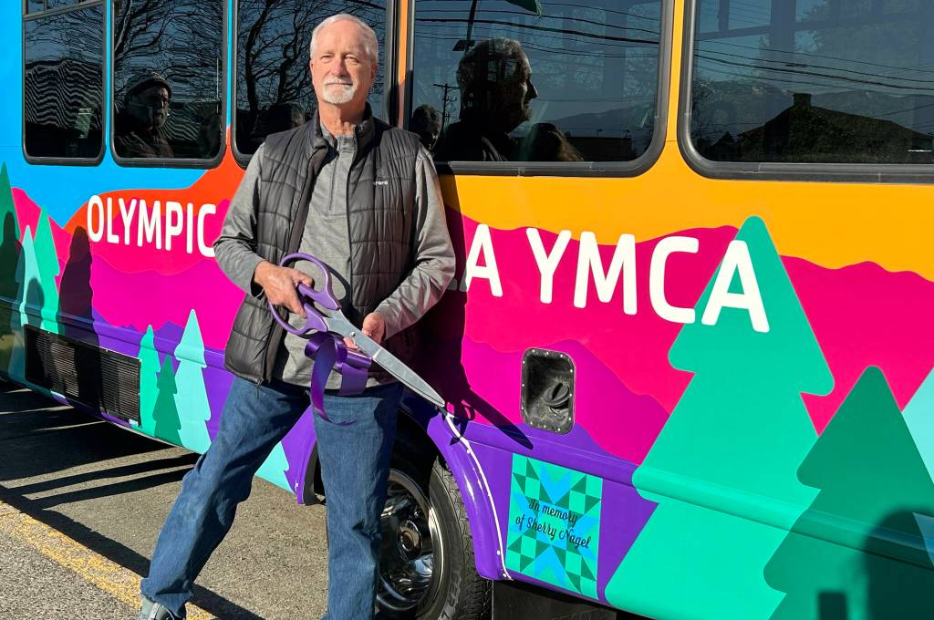 Sequim Gazette photo by Matthew Nash/ Mike Speer of Bonney Lake stands with the new bus his sister Sherry Nagels estate helped pay for at the YMCA of Sequim. A quilt square with a dedication to Nagel is on the side of the bus.