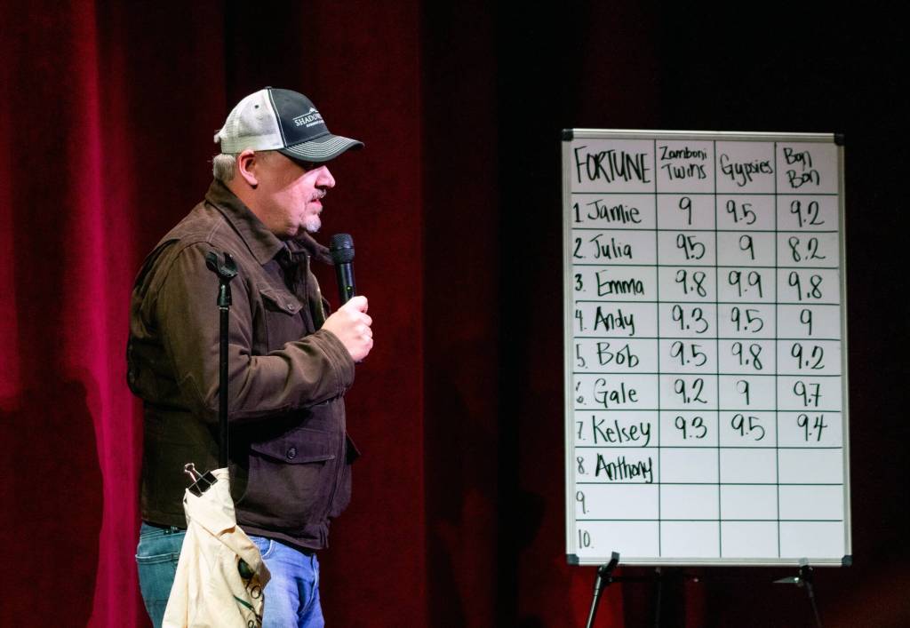 Anthony Richards, textbook artist, shares his story of gratitude next to a whiteboard graph keeping track of storytellers and their scores from three pairs of judges in the audience at Olympic Theatre Arts.