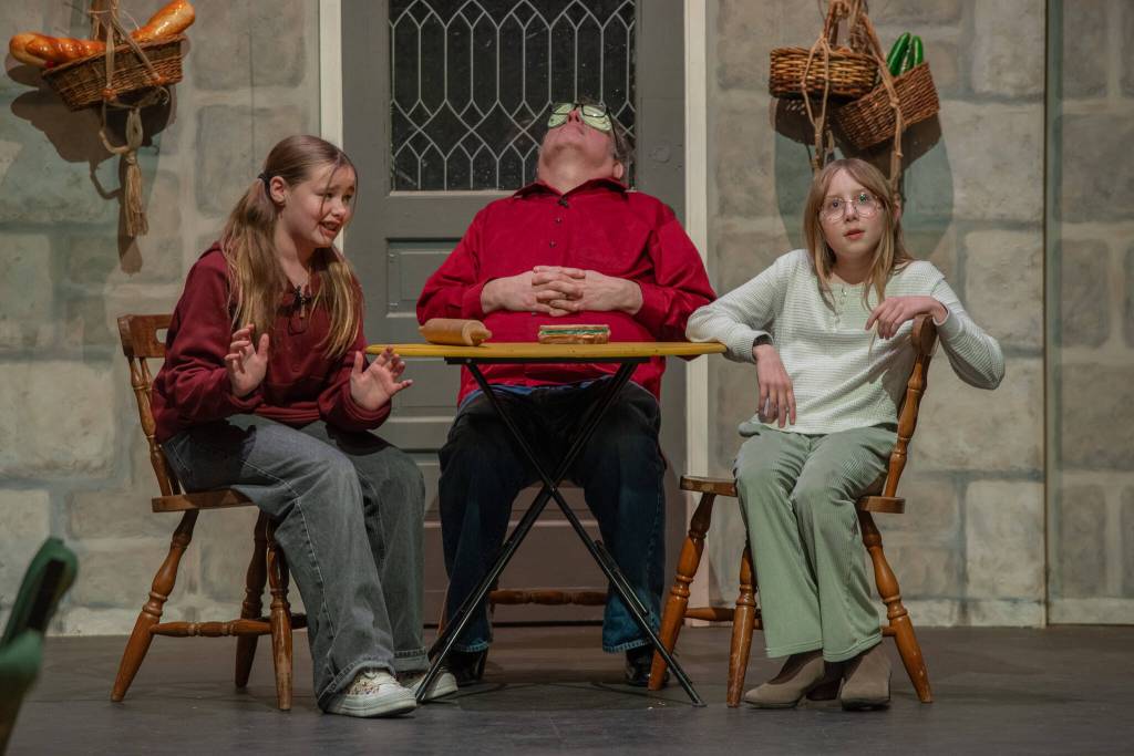 Sequim Gazette photo by Emily Matthiessen/ During a recent non-dress rehearsal, actors Tilly Woods as Cinderella, left, and Rain Nelson as stepsister Druzella discuss a private agreement in the kitchen as the cook, Richard Stephens, takes a snooze in OTAs upcoming Panto Cinderella and the Enabling Habit.