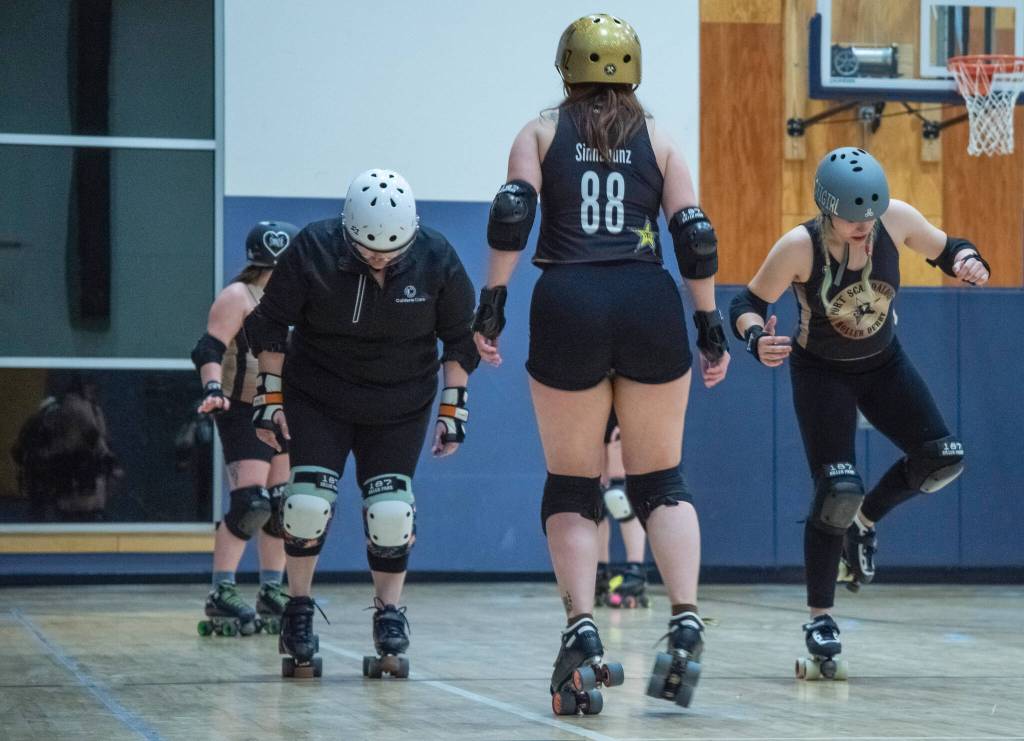 Sequim Gazette photo by Emily Matthiessen/ Port Scandalous Roller Derby skaters practice footwork. We are getting comfortable using our toe stops to quickly shuffle to the side, then back to our wheels. This helps us quickly get around and confuse the blocker who is blocking us, allowing us to create an opening to get past them, explains community outreach liason media liason, Madelyn Doffing, who can seen on one foot to the right.