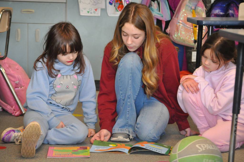 Sequim Gazette photo by Matthew Nash/ Greywolf Elementary second graders Carolyn Keynoyer, left, and Emily Pedrey, on right, read with eighth grader Elizabeth Grimes for Read Across America Day.