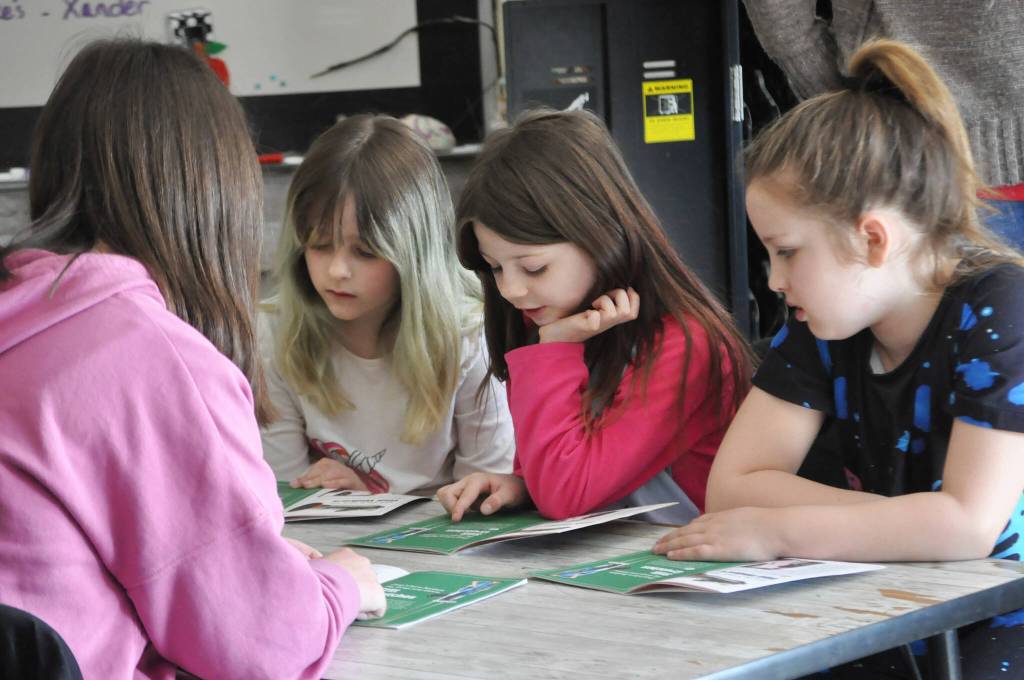 Sequim Gazette photo by Matthew Nash/ Second graders, from left, Envi Chaffin, Stella Mueller and Taelynn Savell reads about inventions with eighth grader Frances Haskins during Read Across America Day in Sequim.