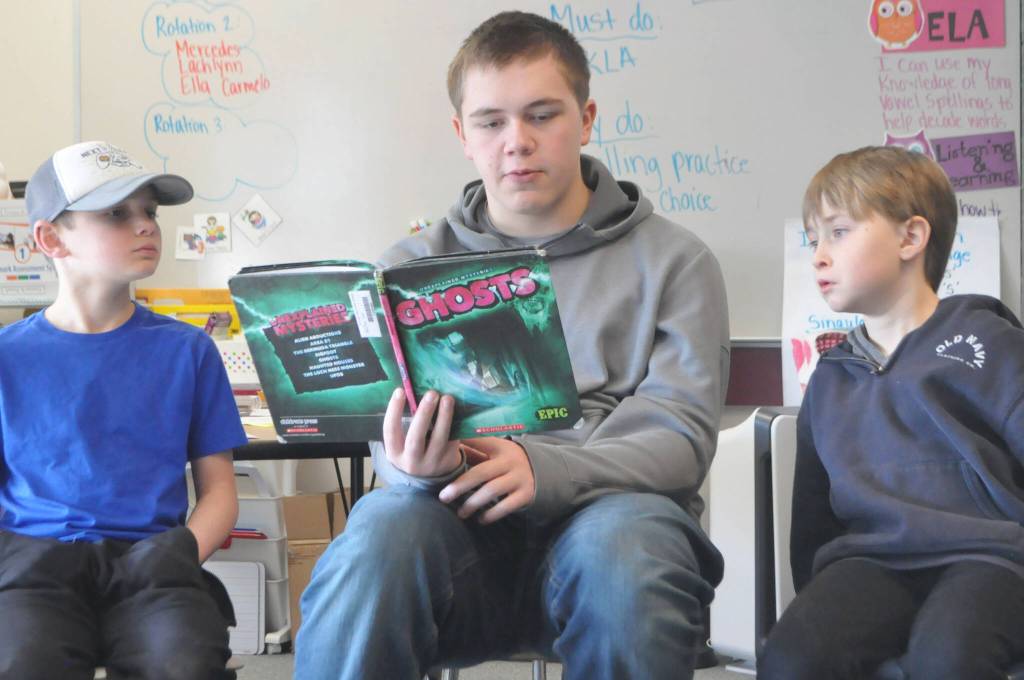 Sequim Gazette photo by Matthew Nash/ Sequim Middle Schooler Cash Hiner reads to Greywolf Elementary students Nickalus Clemmons, on left, and Liam Patterson, right, about unexplained mysteries with ghosts.